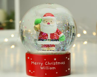 May include: A red snow globe with a Santa Claus figurine inside. The globe has a red base with white stars and the text "Merry Christmas William".