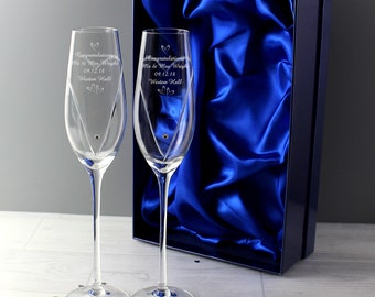 May include: Two clear glass champagne flutes with a diamond-shaped design and a single crystal on the stem. The flutes are engraved with the text "Congratulations Mr & Mrs Wright 09.12.18 Weston Hall" and are displayed in a blue velvet-lined box.