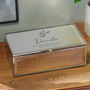 May include: A rectangular mirrored jewellery box. The lid is inscribed with the name "Danielle" in cursive, floral details, and the words "Our Beautiful Daughter Love Mum & Dad". The box is made of glass with a silver-coloured frame.