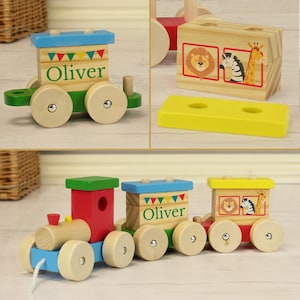 May include: A colourful wooden toy train with a pull string. The train has three carriages, one with the name "Oliver" on it, one with a lion, zebra, and giraffe, and one with a red roof. The train is on a wooden floor.