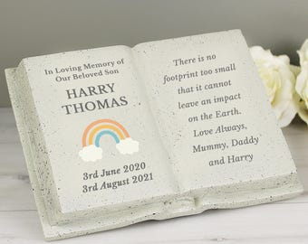 May include: A light gray, open book-shaped memorial. The left page reads "In Loving Memory of Our Beloved Son, HARRY THOMAS" with a rainbow graphic. The right page reads "There is no footprint too small...Love Always, Mummy, Daddy and Harry."