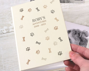 May include: A cream-colored photo album with a paw print and bone pattern. The album is titled "Rory's Adventures 2008-2023".