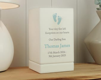 May include: White ceramic keepsake box with a blue footprint design. The box has the text "Your tiny feet left footprints on our hearts Our Darling Son Thomas James 17th March 2024 - 9th January 2025"