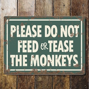 May include: A green metal sign with white text that reads "Please do not feed or tease the monkeys". The sign has a rustic, weathered look.