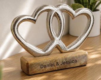 May include: A decorative sculpture featuring two interlocking silver-colored hearts with a textured metallic finish. The hearts are mounted on a rectangular wooden base with the engraved text "Daniel & Jessica" centered on the front face.
