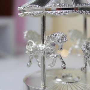 Peut inclure: Un carrousel argent&eacute; avec trois chevaux, un toit argent&eacute; et une base argent&eacute;e. Le carrousel est un objet d&eacute;coratif.