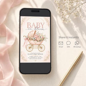 May include: A smartphone displaying a digital baby shower invitation with the text BABY in bloom, featuring a pink vintage baby carriage filled with flowers, gold wheels, and event details for Olivia's baby shower on Sunday, June 14 at 2 PM.