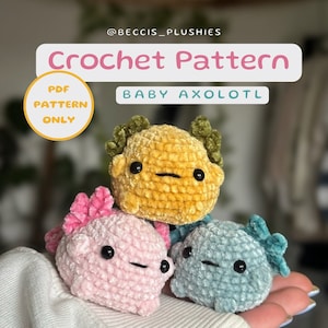 Può includere: Schema all'uncinetto per un baby axolotl. Lo schema è disponibile solo come download PDF. L'immagine mostra tre axolotl all'uncinetto in rosa, blu e giallo.