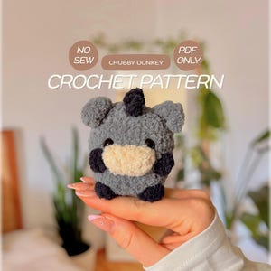 Könnte beinhalten: Ein kleiner, grauer, plüschiger Häkel-Esel mit cremefarbener Schnauze, schwarzen Hufen und einer schwarzen Haarbüschel auf dem Kopf. Der Text auf dem Bild lautet NO SEW, CHUBBY DONKEY, PDF ONLY und CROCHET PATTERN in runden Beschriftungen.