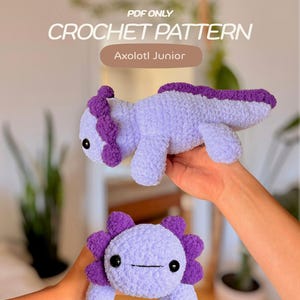 Könnte beinhalten: Eine PDF-Häkelanleitung für einen Axolotl Junior. Das Bild zeigt zwei gehäkelte Axolotl-Stofftiere aus hellviolettem Garn mit dunkelvioletten Akzenten an den Kiemen und der Rückenflosse. Beide Figuren haben schwarze Kunststoff-Sicherheitsaugen.