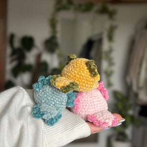 Peut inclure: Trois petites figurines axolotl en crochet, de couleur bleu clair, jaune moutarde et rose tendre. Chaque cr&eacute;ature pr&eacute;sente un corps arrondi, une surface en fil textur&eacute; et des branchies externes distinctes dans une teinte plus fonc&eacute;e.