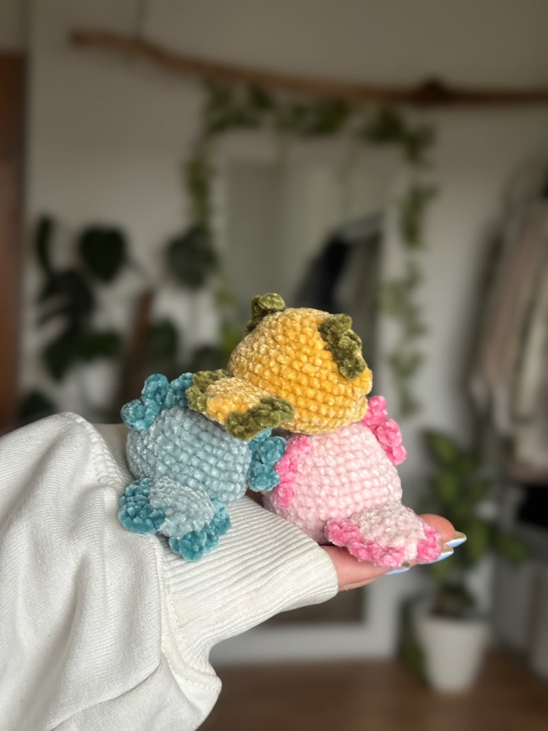 Peut inclure: Trois petites figurines axolotl en crochet, de couleur bleu clair, jaune moutarde et rose tendre. Chaque cr&eacute;ature pr&eacute;sente un corps arrondi, une surface en fil textur&eacute; et des branchies externes distinctes dans une teinte plus fonc&eacute;e.
