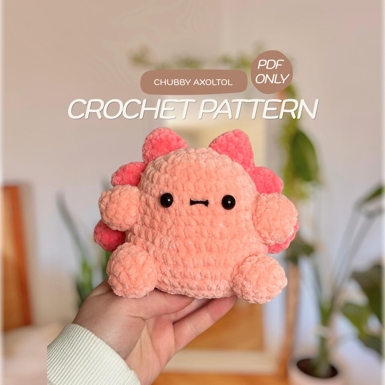 May include: A plush, light pink crochet axolotl toy with dark pink frills, black bead eyes, and a small stitched mouth. The image includes text that reads CHUBBY AXOLTOL and PDF ONLY CROCHET PATTERN in white and brown graphic elements.