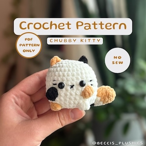 Könnte beinhalten: Häkelanleitung für ein kuscheliges Kätzchen ohne Nähen. Die Anleitung ist nur als PDF-Download erhältlich. Das Kätzchen ist weiß mit schwarzen und orangen Akzenten.