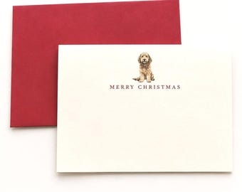 Könnte beinhalten: Eine cremefarbene Grußkarte mit einer kleinen Illustration eines goldbraunen Hundes mit rotem Halsband, darunter der in Rot gedruckte Text MERRY CHRISTMAS, sowie ein passender dunkelroter Umschlag, der hinter der Karte platziert ist.