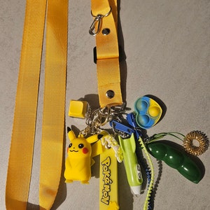 Puede incluir: Un cordón amarillo con un amuleto de Pikachu, un juguete para fidget verde y azul, un tirador de cremallera verde y azul, un bolígrafo verde, un tirador de cremallera amarillo y verde y un amuleto amarillo "Pokémon".