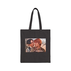 May include: Black tote bag featuring a romantic illustration of two people embracing. The image includes the text "the NEXT PRINCE" in a small font. The bag has two black handles.