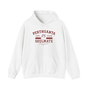 Puede incluir: Sudadera con capucha blanca con bolsillo delantero y cordón. La sudadera presenta el texto "PERTHSANTA" sobre "SOULMATE Program" en granate, con "EST PS 2024" encima. Una prenda casual y cómoda.