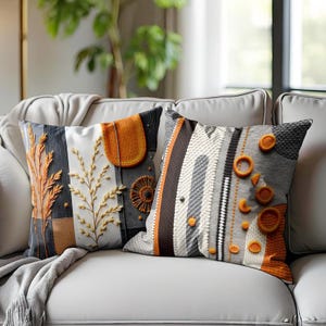 Può includere: Due cuscini decorativi con motivi astratti. Un cuscino presenta un design geometrico con strisce arancioni e grigie. L'altro cuscino ha un design più organico con accenti arancioni e bianchi.