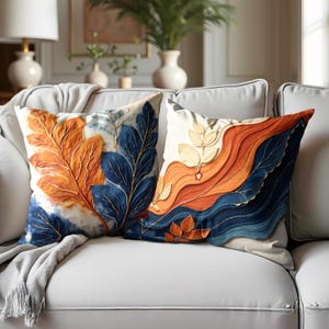 Può includere: Due cuscini decorativi con motivi di foglie astratte. Un cuscino presenta foglie blu e arancioni, mentre l'altro ha un design blu, arancione e bianco.