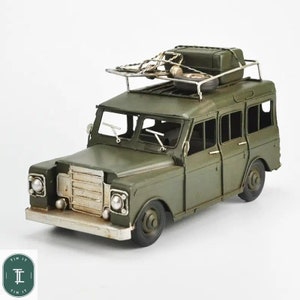 May include: A green metal toy model of a vintage safari jeep with a roof rack and a small motorcycle on top. The jeep has a spare tire on the back and a detailed front grill.