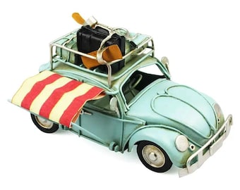 May include: A light blue vintage car model with a striped beach towel and luggage on the roof rack. The car has a detailed design and a weathered finish.