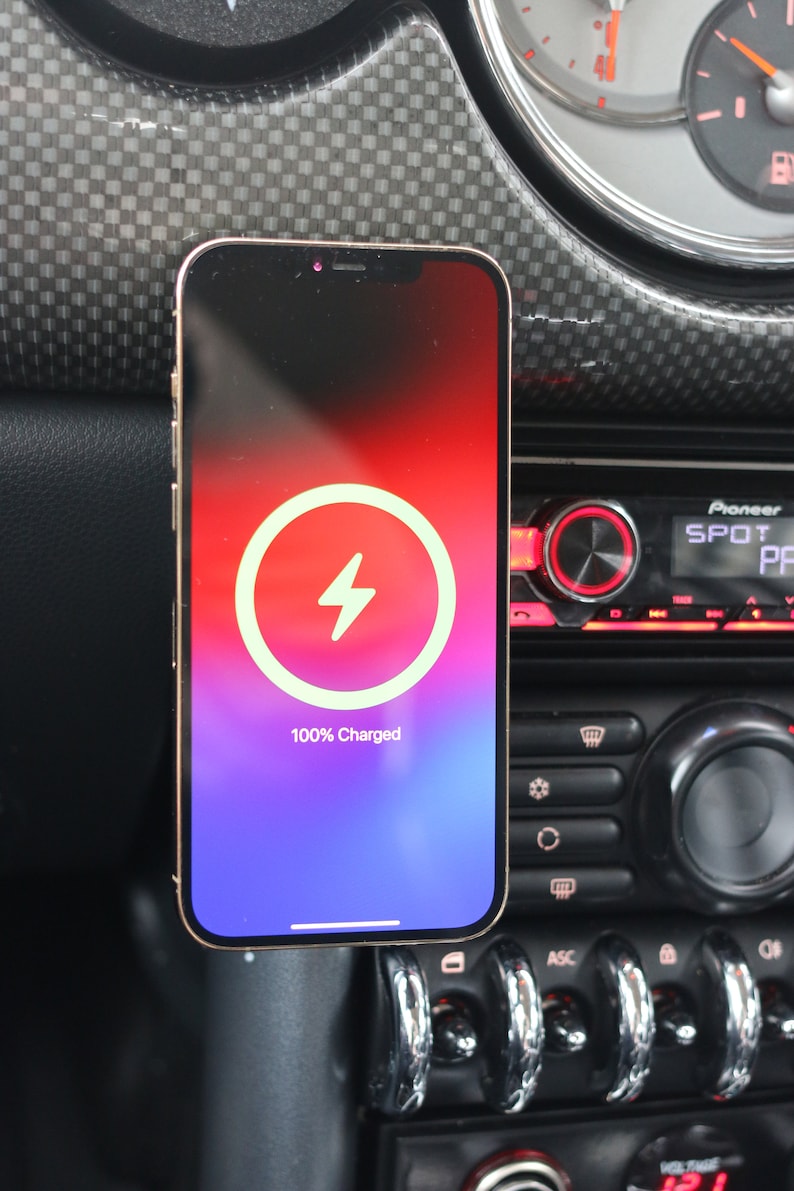 Peut inclure: Un iPhone dor&eacute; avec une ic&ocirc;ne de charge blanche sur un &eacute;cran d&eacute;grad&eacute; violet et rouge. Le t&eacute;l&eacute;phone est mont&eacute; dans une voiture et affiche "100% charg&eacute;".