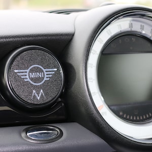 Peut inclure: Tableau de bord de voiture noir avec un compteur rond et un emblème circulaire "MINI". Le compteur affiche la vitesse et d'autres informations du véhicule. Détails argentés.