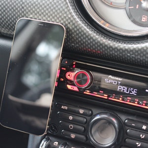 Peut inclure: Un smartphone noir est mont&eacute; sur le tableau de bord d'une voiture, &agrave; c&ocirc;t&eacute; d'un autoradio Pioneer avec le mot "PAUSE" affich&eacute; &agrave; l'&eacute;cran.
