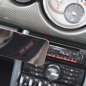 Peut inclure: Un tableau de bord de voiture noir avec un support de t&eacute;l&eacute;phone noir et un autoradio noir avec un &eacute;cran num&eacute;rique affichant "SPOT PAUSE".