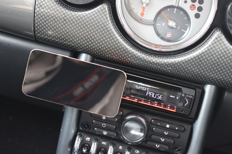 Peut inclure: Un tableau de bord de voiture noir avec un support de t&eacute;l&eacute;phone noir et un autoradio noir avec un &eacute;cran num&eacute;rique affichant "SPOT PAUSE".