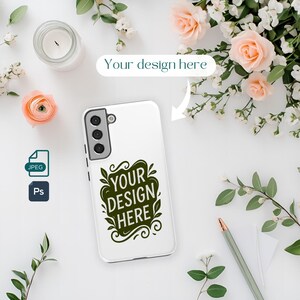以下が含まれることがあります： 「Your Design Here」と書かれた濃い緑色のデザインの白いスマートフォンケース。スマートフォンケースにはカメラとフラッシュが付いています。画像には花、ろうそく、鉛筆も含まれています。