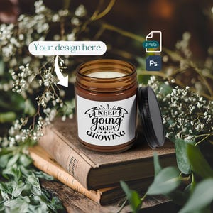 Puede incluir: Un tarro de vela de vidrio marrón con una etiqueta blanca que dice "Keep going keep growing". La vela está sentada sobre una pila de libros viejos con una planta verde frondosa en el fondo.