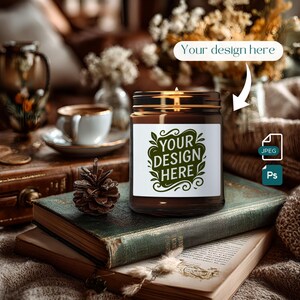 Op de afbeelding: Een bruine glazen kaarsenpot met een gouden deksel en een wit etiket met de groene tekst "YOUR DESIGN HERE". De kaars staat op een vintage boek. Een dennenappel en een theekopje staan op de achtergrond.