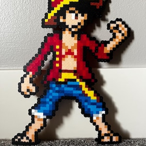 May include: A pixel art figure of a cartoon character wearing a red shirt, blue shorts, and a straw hat with a yellow band. The character has black hair and is in a fighting pose.