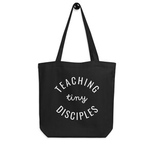 May include: Black tote bag with white text that reads "TEACHING tiny DISCIPLES".