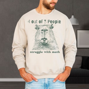 May include: A beige sweatshirt with a green graphic of a capybara and the text "4 out of 3 People struggle with math".