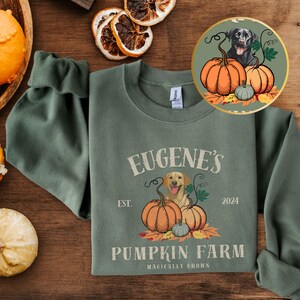 May include: A green sweatshirt with a pumpkin farm logo. The logo features a golden retriever dog, pumpkins, and the text "Eugene's Pumpkin Farm, Est. 2024, Magically Grown".