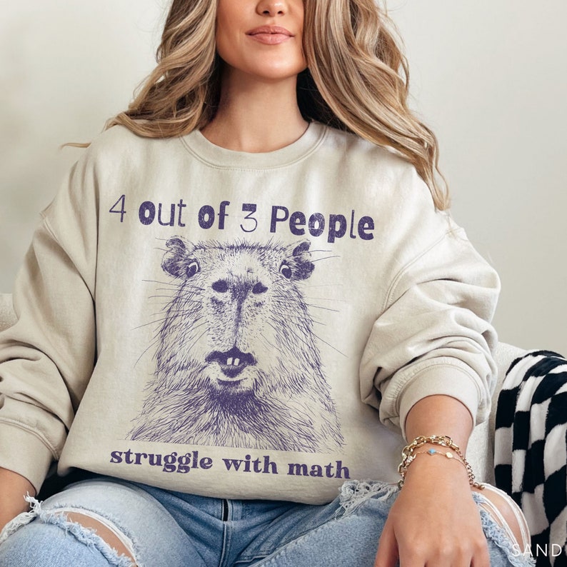 May include: A light beige sweatshirt with a purple graphic of a capybara and the text "4 out of 3 People struggle with math".
