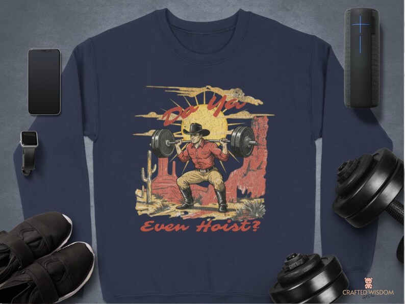 May include: Navy blue sweatshirt featuring a weightlifting cowboy graphic. The design includes a cowboy lifting a barbell with the text "Do You Even Hoist?" in a vintage style. The sweatshirt is surrounded by workout equipment.