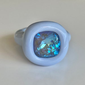 May include: A light blue ring with a large, square-shaped, iridescent blue gemstone set in a white ceramic bezel.