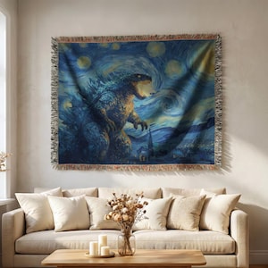 May include: A woven tapestry featuring a Godzilla design in the style of Van Gogh's "Starry Night." The artwork depicts Godzilla with an open mouth against a swirling blue and yellow night sky. The tapestry has a fringed edge.