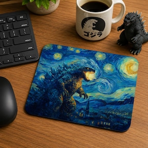 May include: A rectangular mousepad featuring a stylized image of Godzilla in a starry night setting. The design incorporates shades of blue, yellow, and white, with the monster's mouth emitting a bright glow. A black keyboard, mouse, and coffee mug are also visible.