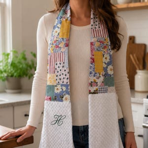 May include: A hanging kitchen towel featuring a patchwork fabric top section with various floral, striped, and solid patterns in yellow, blue, pink, and white. The bottom section is a white waffle-textured fabric with a dark green embroidered letter H.
