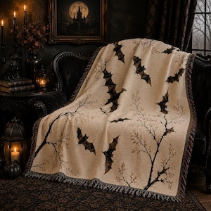 Peut inclure: Un plaid tissé de couleur beige clair présentant un motif répétitif de chauves-souris brunes en vol et de branches d'arbres dénudées et fines. La couverture possède une finition en tissu texturé et un bord frangé sur la partie inférieure.