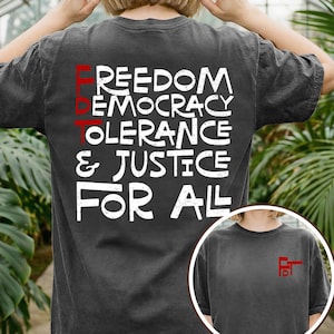 Op de afbeelding: Donkergrijs t-shirt met de woorden "FREEDOM, DEMOCRACY, TOLERANCE & JUSTICE FOR ALL" in het wit, en "FDT" in het rood. Een kleinere afbeelding van het shirt staat rechtsonder, met het rode "FDT" logo.