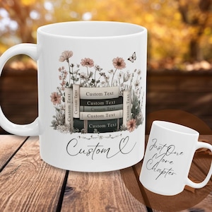 May include: White ceramic mug with a floral design, a stack of books, and the words "Custom Text". A smaller mug displays "Just One More Chapter". The mugs are on a wooden surface.