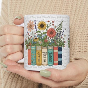 May include: White ceramic mug featuring a floral design with colorful flowers and books. The books have the words "Foxtrot", "Delta", and "Tango" on them. The mug also has the words "Donald Trump Fuck" printed on it.