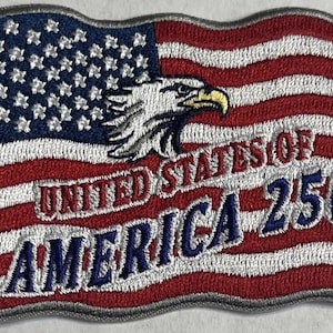 May include: A rectangular embroidered patch featuring a wavy American flag design with a white bald eagle head in the center. The text UNITED STATES OF AMERICA 250 is stitched in red and blue thread across the center of the flag design.