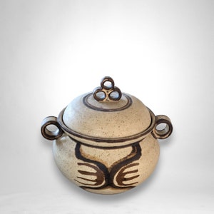 Op de afbeelding: Een witte, gedekte keramische schaal met een bruin gespikkeld glazuur en een bruin abstract ontwerp. Het deksel heeft drie bruine lussen als handvatten.